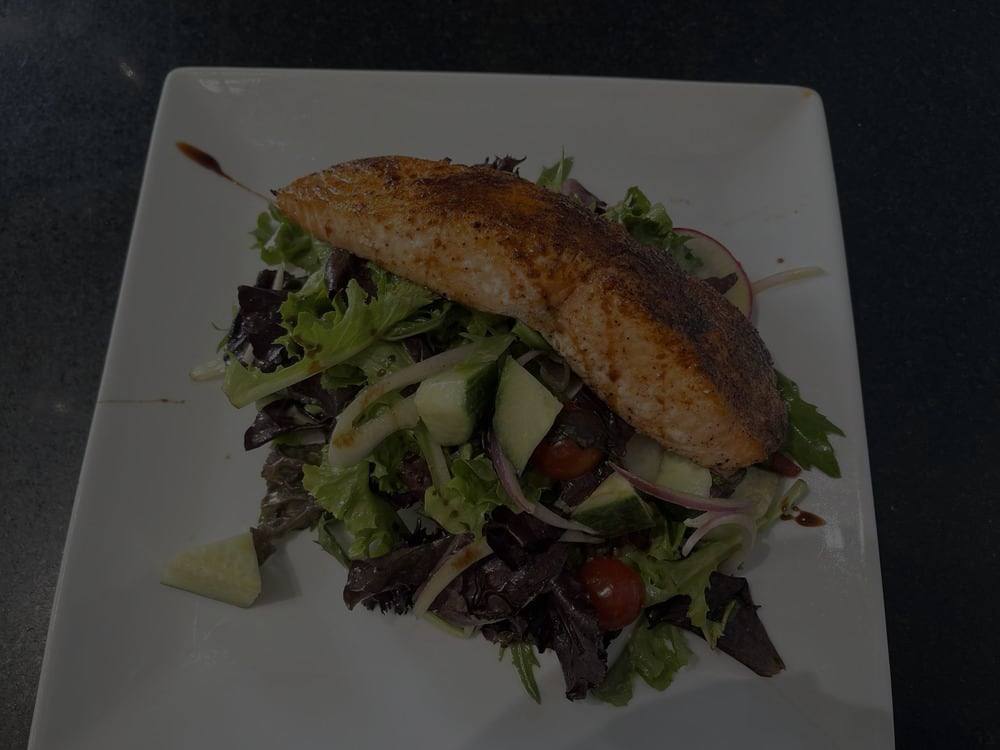 A seared fish fillet over mixed greens with cucumber, tomato and red onion
