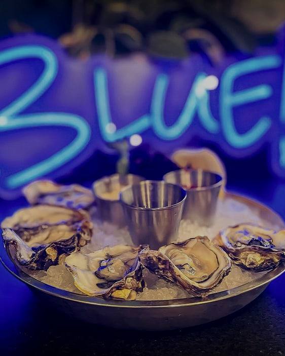 Oysters on the half shell on a platter of ice with sauce cups, lit by a blue neon sign