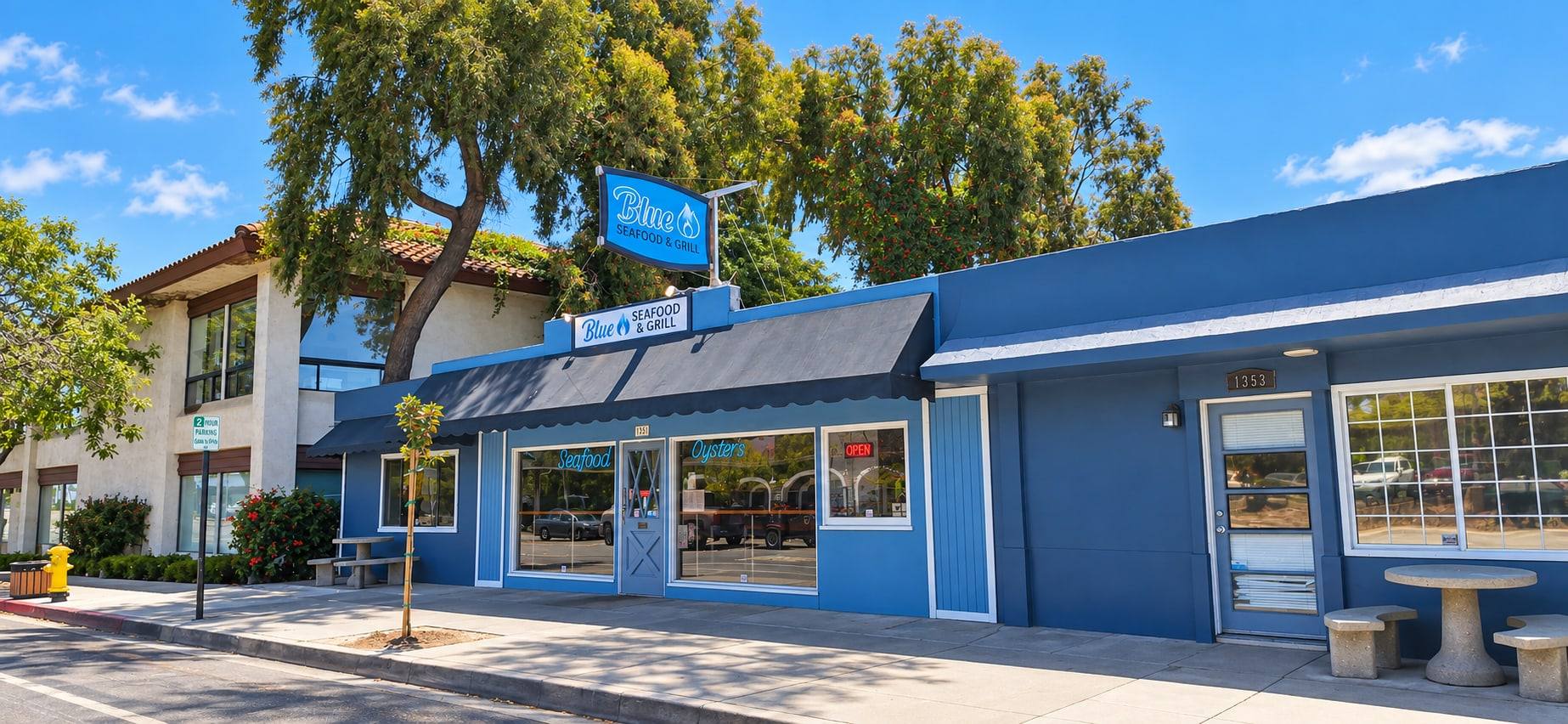 The blue Blue Seafood & Grill storefront at 1351 E Grand Ave on a sunny day, with the Blue sign above the awning and “Seafood” and “Oysters” neon in the front windows
