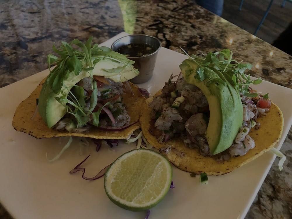 Two tostadas topped with avocado, microgreens and a wedge of lime